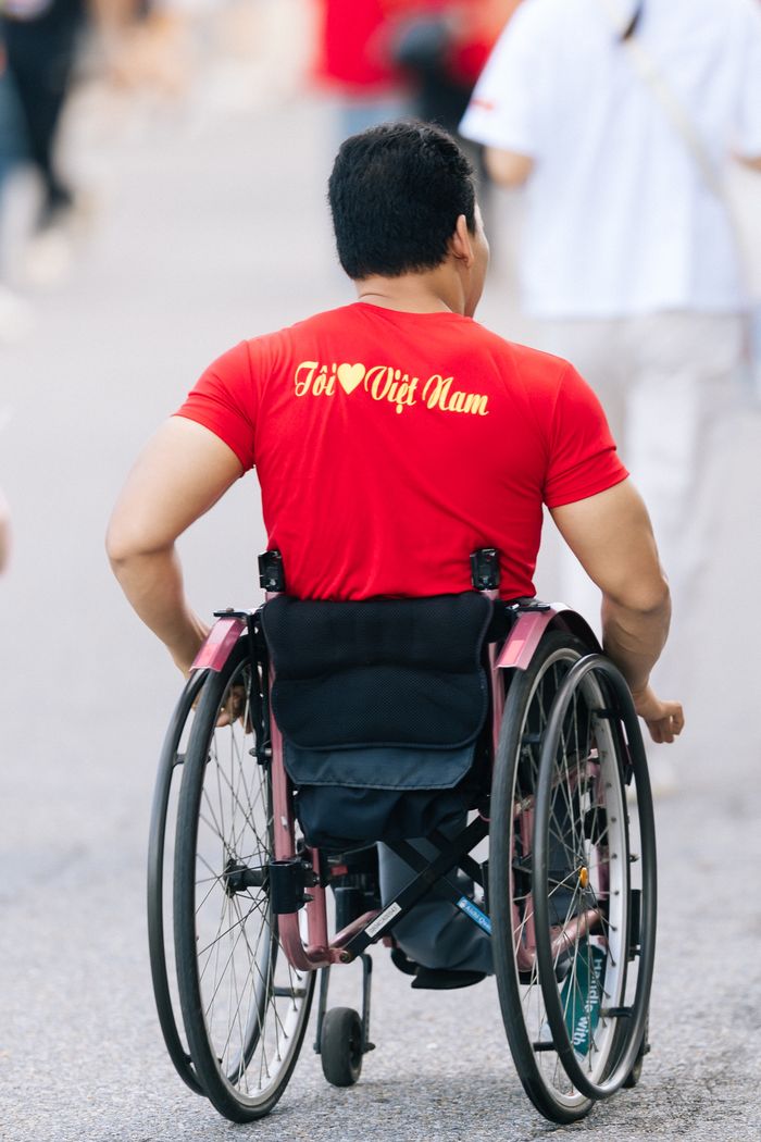 Man in a red shirt, promoting Vietnam, in a wheelchair on a busy street.