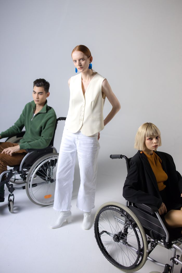 Three individuals in stylish attire, featuring two in wheelchairs, on a white backdrop.